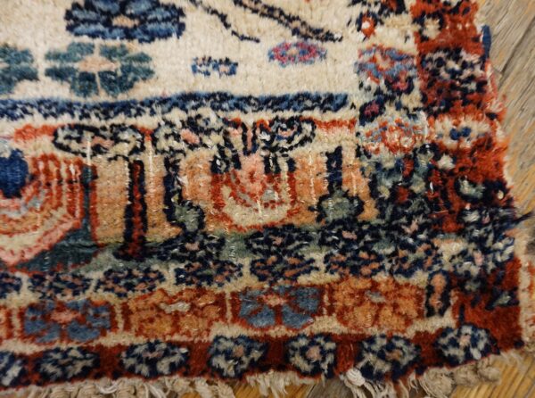 Detailed view of a shaggy rug border with red, blue, cream, and green traditional motifs over wood planks.