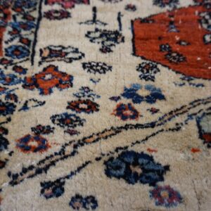 Textured beige rug with medium pile, featuring traditional floral motifs in red, navy blue, and black.