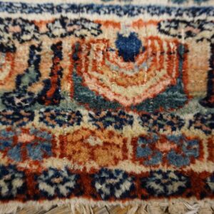 Intricate woven design in rust, navy, and cream with a textured pile and visible fringe edge.