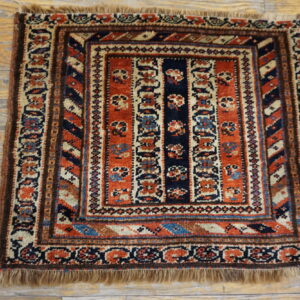 Low-pile square rug with intricate rust, navy, and cream geometric designs on wooden plank flooring.