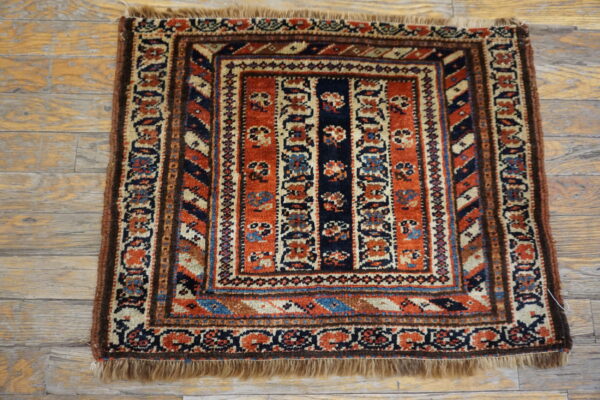 Low-pile square rug with intricate rust, navy, and cream geometric designs on wooden plank flooring.