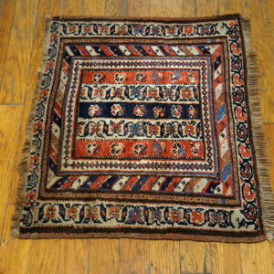 Low-pile square rug with intricate rust, navy, and tan traditional patterns on a wooden floor.
