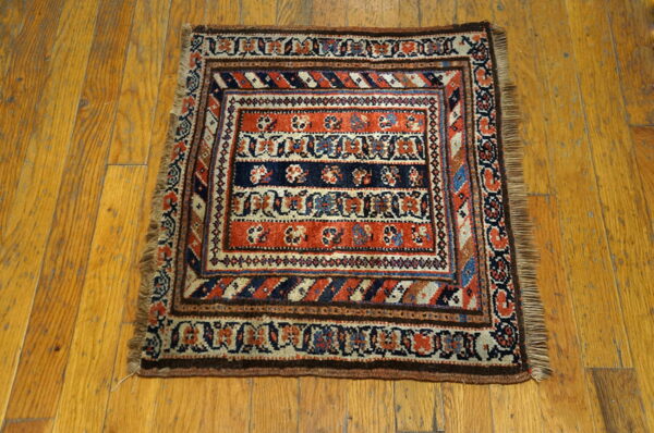 Low-pile square rug with intricate rust, navy, and tan traditional patterns on a wooden floor.