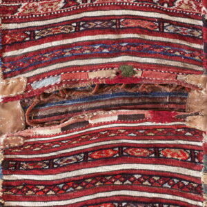 Distressed woven textile featuring bold red, ivory, and dark geometric stripes with visible central repairs and patches.