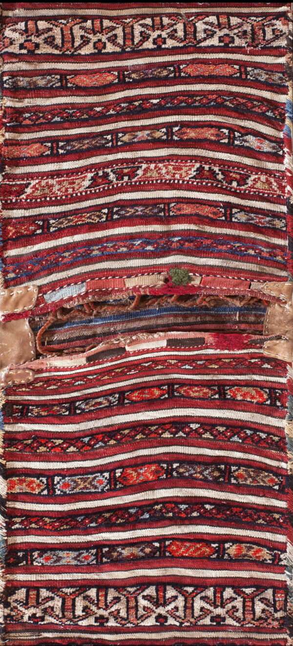 Distressed woven textile featuring bold red, ivory, and dark geometric stripes with visible central repairs and patches.