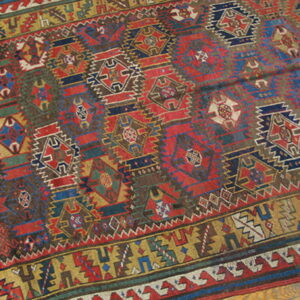 Complex geometric rug featuring red, navy, brown, and mustard yellow medallions resting on a hardwood floor.