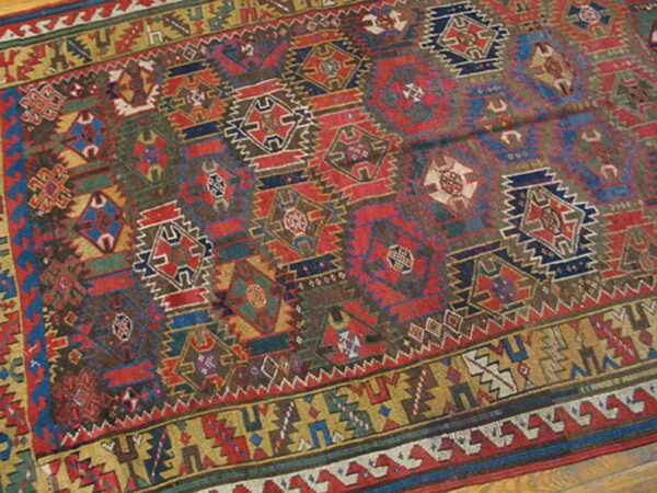 Complex geometric rug featuring red, navy, brown, and mustard yellow medallions resting on a hardwood floor.