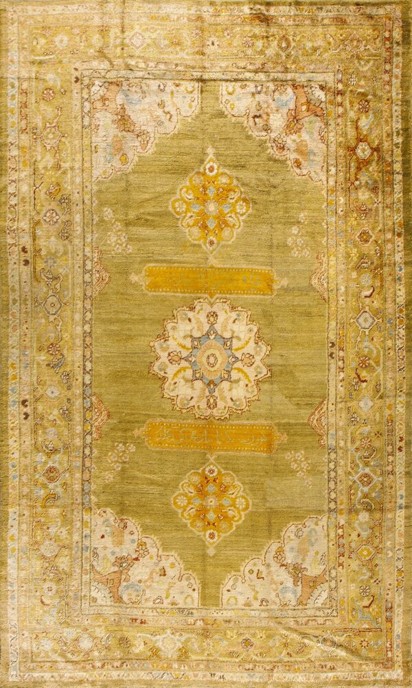 Full view of an olive green rug with visible abrash, detailed floral borders, and gold central medallions.