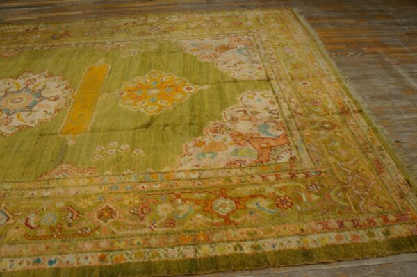 Lime green ornate rug with yellow, peach, and blue accents lying on light brown wood plank flooring.