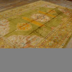 Striated olive rug with yellow and pink traditional designs lying on a distressed hardwood floor.