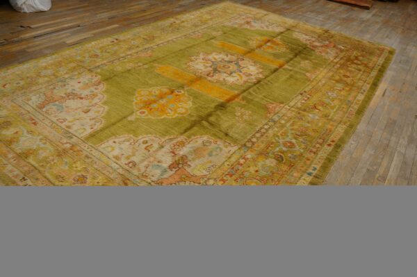 Striated olive rug with yellow and pink traditional designs lying on a distressed hardwood floor.