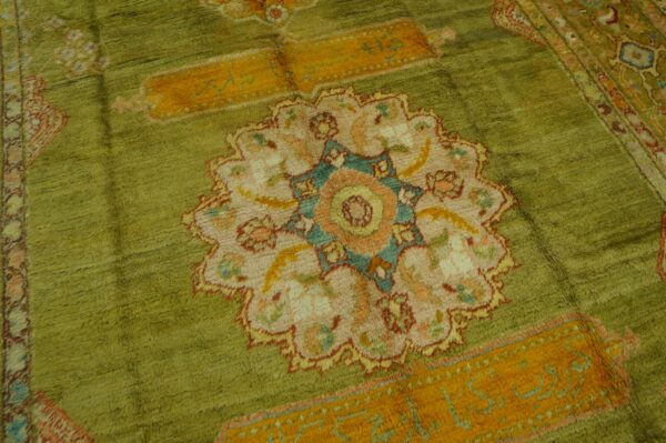 High-pile olive green rug displaying a central medallion design with orange, pink, cream, and teal accents.