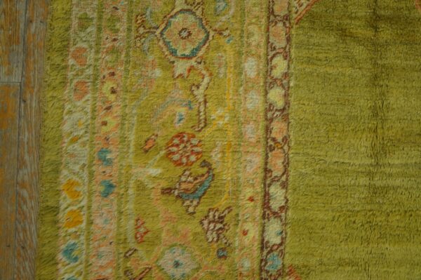 Textured chartreuse rug featuring multicolored traditional patterns next to distressed wood plank flooring.