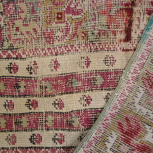Close-up of a low-pile rug featuring striped bands of beige, magenta, black, and green geometric patterns.