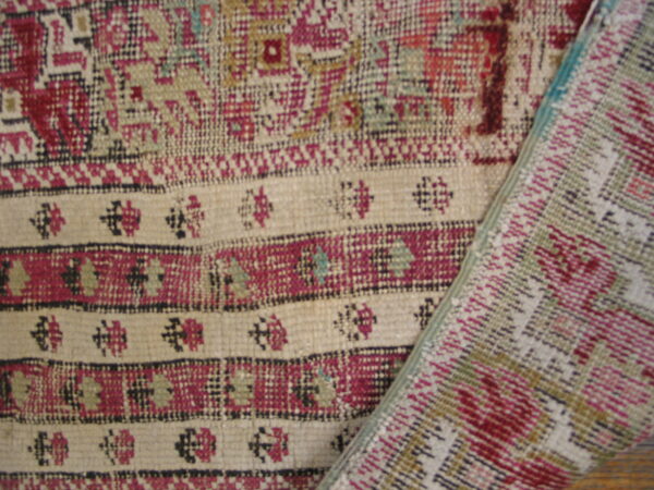 Close-up of a low-pile rug featuring striped bands of beige, magenta, black, and green geometric patterns.
