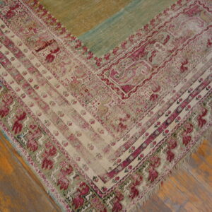 Distressed rug corner featuring magenta and cream geometric borders next to distressed green and tan panels on wood floor.