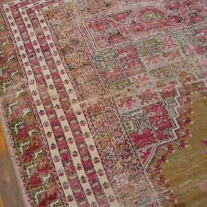Close-up of a worn geometric rug in magenta, cream, and olive green on natural wood flooring.