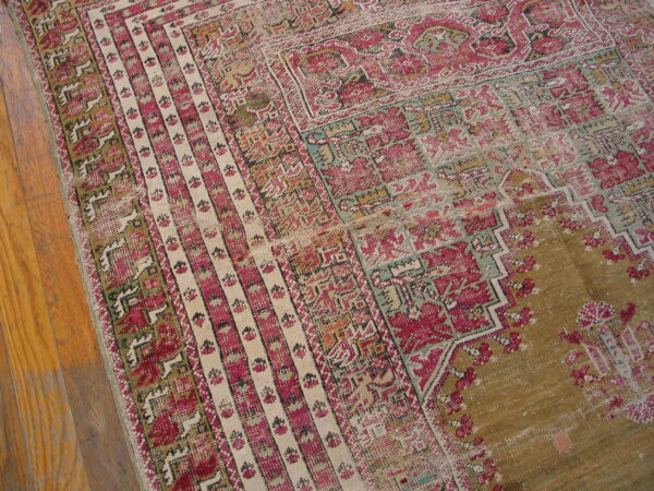Close-up of a worn geometric rug in magenta, cream, and olive green on natural wood flooring.