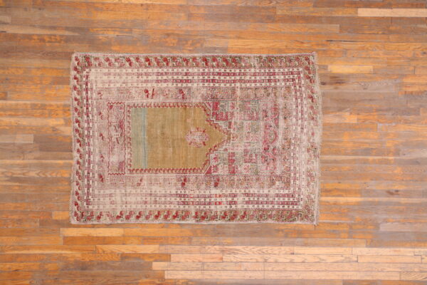 Low-pile rug with red and beige geometric borders and a gold-tan field rests on wood flooring.