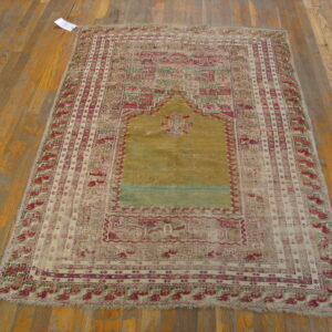 Faded, low-pile rug with a central gold mihrab pattern and magenta borders on worn wooden flooring.