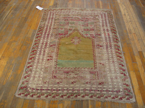 Faded, low-pile rug with a central gold mihrab pattern and magenta borders on worn wooden flooring.