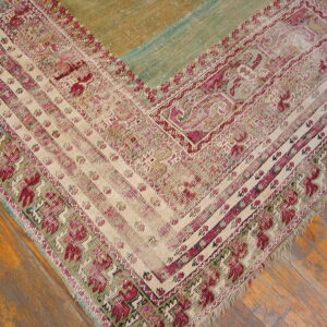 Low-pile rug corner in cream, magenta, and muted green with a color-blocked field rests on wood planks.