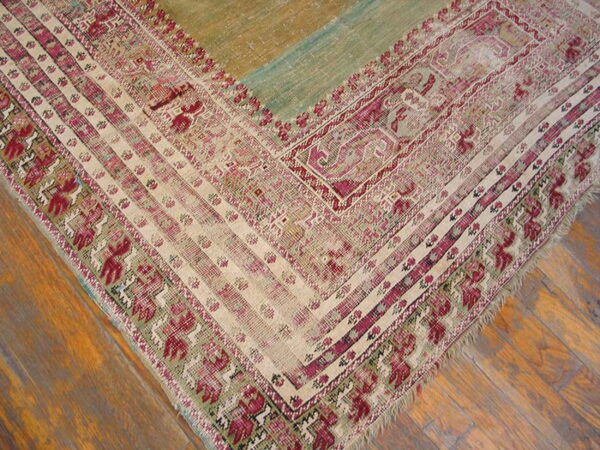 Low-pile rug corner in cream, magenta, and muted green with a color-blocked field rests on wood planks.