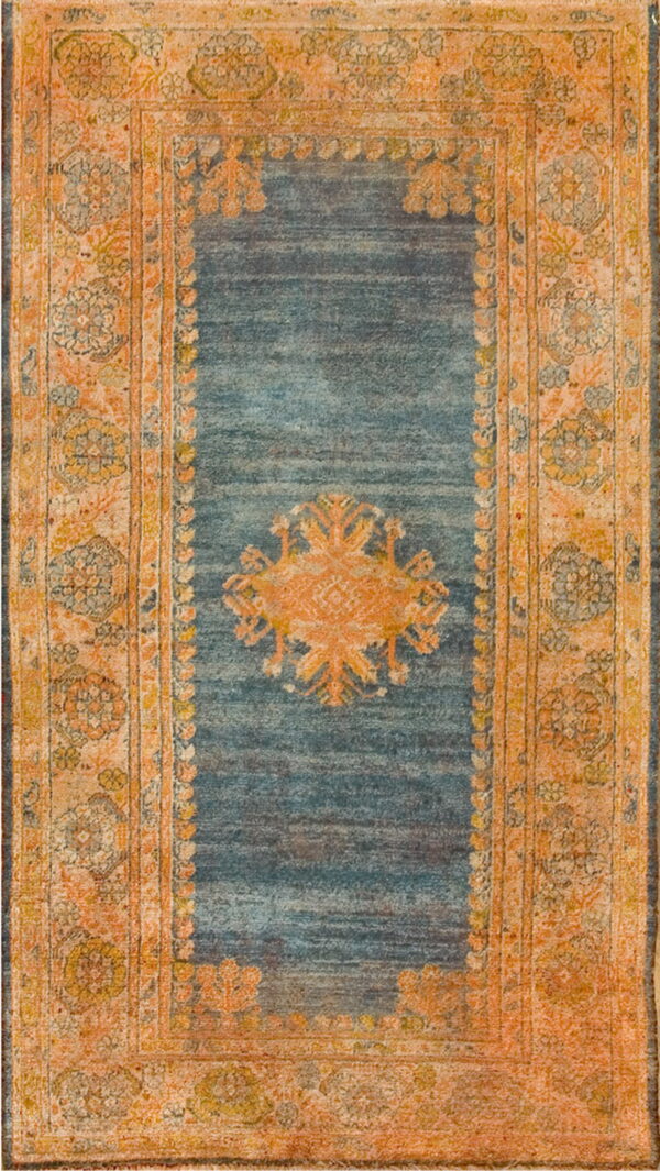 A distressed blue rug with a fading orange central medallion and wide patterned border.