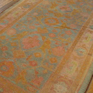 A distressed low-pile rug in muted coral, teal, and gold with a floral pattern laid on wood floors.