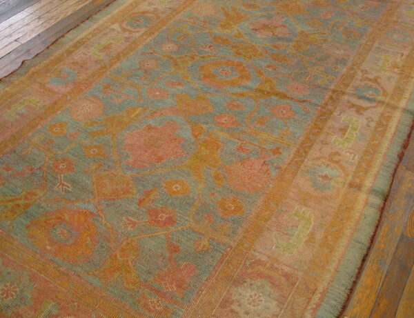 A distressed low-pile rug in muted coral, teal, and gold with a floral pattern laid on wood floors.