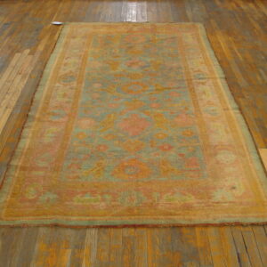 Muted teal and coral patterned rug with low pile lying on aged wooden plank flooring.