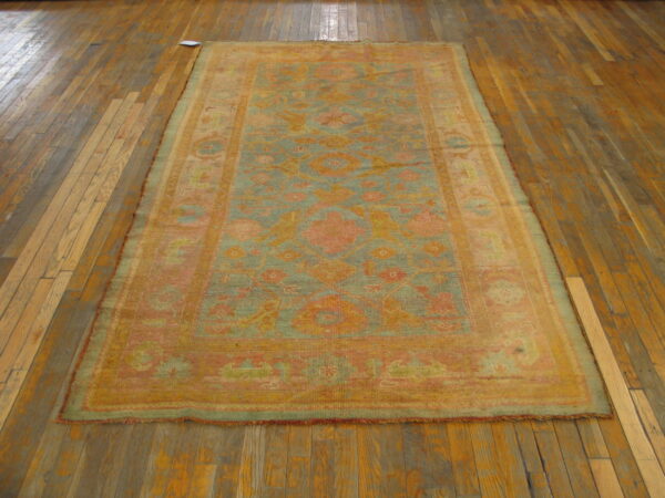 Muted teal and coral patterned rug with low pile lying on aged wooden plank flooring.