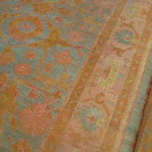 Faded low pile rug featuring teal, coral, and gold traditional patterns borders dark hardwood flooring.