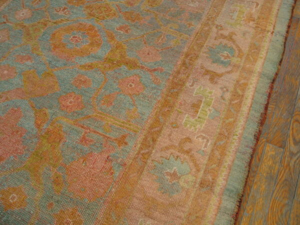 Faded low pile rug featuring teal, coral, and gold traditional patterns borders dark hardwood flooring.