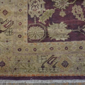 Intricate low-pile rug in tan and burgundy with floral motifs rests on worn wooden floorboards.