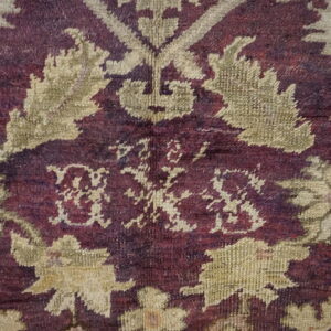 Detailed view of a deep purple and beige patterned rug with a central stylized monogram.