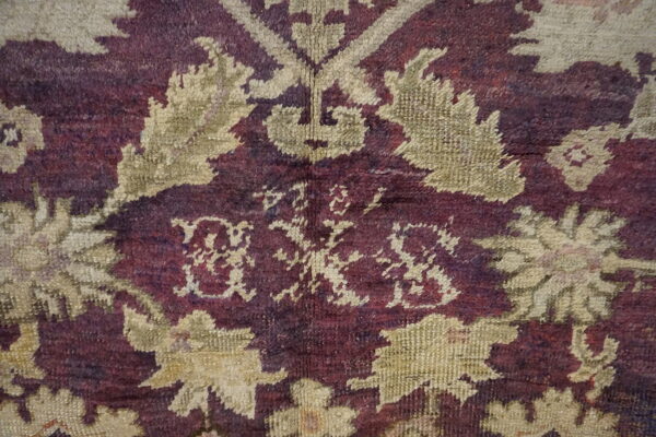 Detailed view of a deep purple and beige patterned rug with a central stylized monogram.