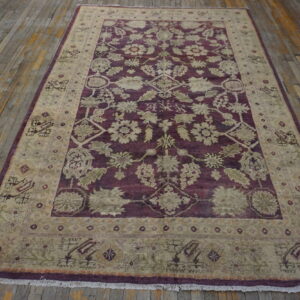 A burgundy and taupe rug featuring an elaborate floral pattern rests on distressed wooden flooring.
