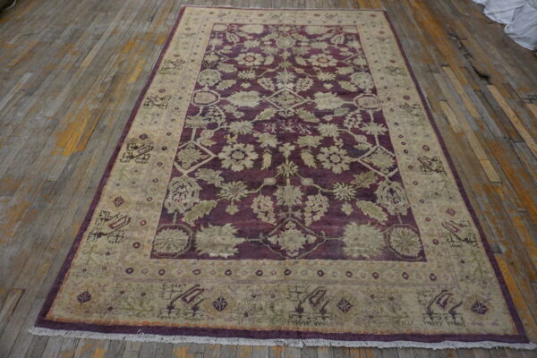 A burgundy and taupe rug featuring an elaborate floral pattern rests on distressed wooden flooring.
