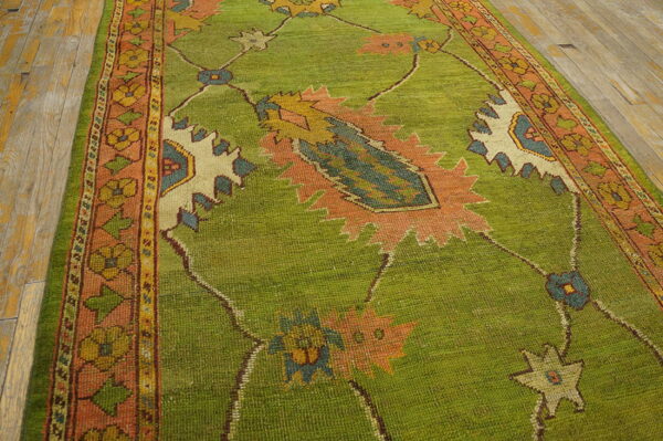 Bright green runner rug with salmon borders and large motifs on worn wood flooring.