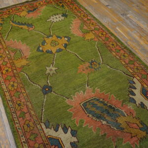 Textured bright green runner rug featuring large coral, blue, and yellow geometric motifs on worn wood flooring.