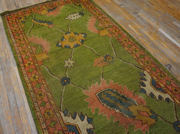 Textured bright green runner rug featuring large coral, blue, and yellow geometric motifs on worn wood flooring.