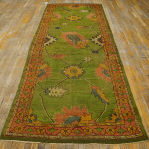 A green runner rug with colorful medallions and an orange border lies on worn wooden floorboards.