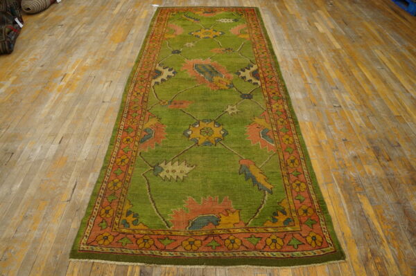 A green runner rug with colorful medallions and an orange border lies on worn wooden floorboards.