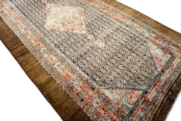 An oblong traditional rug featuring a dark diamond pattern field with coral and teal patterned borders.
