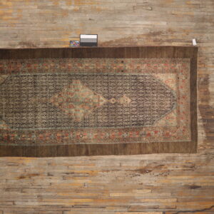 Antique style rug with a brown geometric field, bordered by teal and rust accents on wood floor.