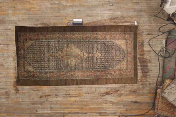 Antique style rug with a brown geometric field, bordered by teal and rust accents on wood floor.