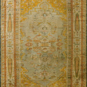 Rectangular traditional rug featuring a pale sage green field, mustard yellow designs, and rust orange borders.