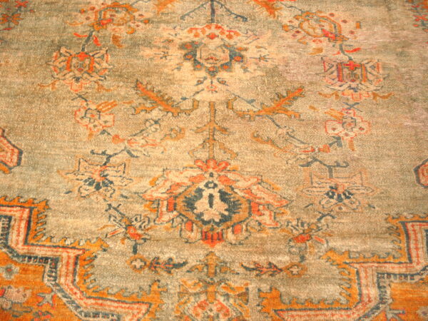 Distressed low-pile rug featuring a traditional orange, navy, and beige pattern on a gray-green field.