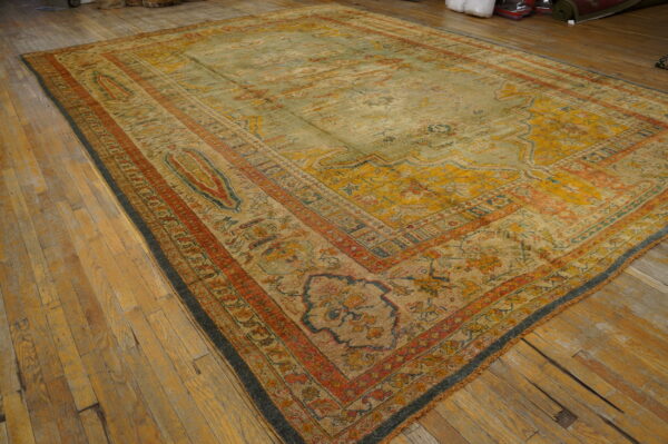 Low-pile traditional area rug in faded sage green, gold, and red hues on distressed wood flooring.